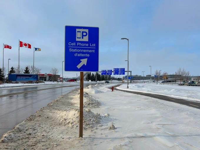 This post shows a cell phone lot street sign with the Winnipeg Richardson International Airport campus in the background. 
