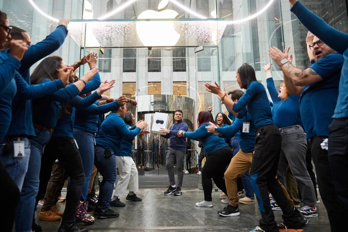A customer holding up their Apple Vision Pro outside of Apple Fifth Avenue, surrounded by retail team members.