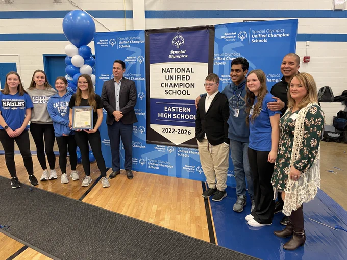 Students and adults pose by a banner that says "Special Olympics, National Unified Champion School, Eastern High School, 2022-2026"