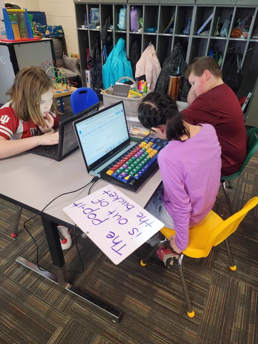 Student using adapted keyboard, whiteboard, and chromebook to write a story. 