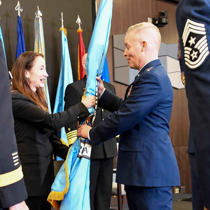 A smiling woman passes a flag to a man in uniform.