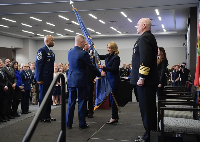A woman passes a flag to a man in uniform, while others look on.