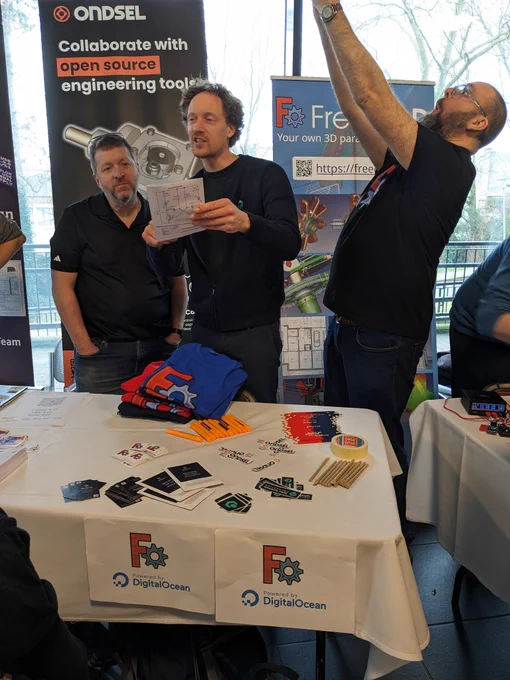 The FreeCAD booth at FOSDEM, with participants in dynamic poses in front of signage.