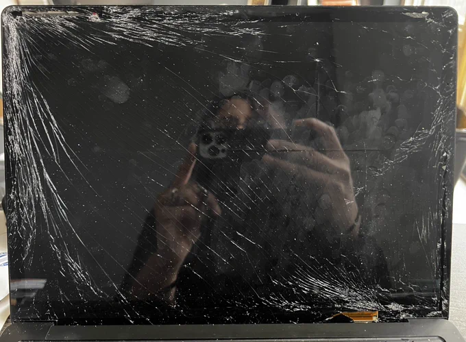 A computer screen that is cracked in so many places. The reflection of the person taking the picture can be seen in between all the cracks. 💻