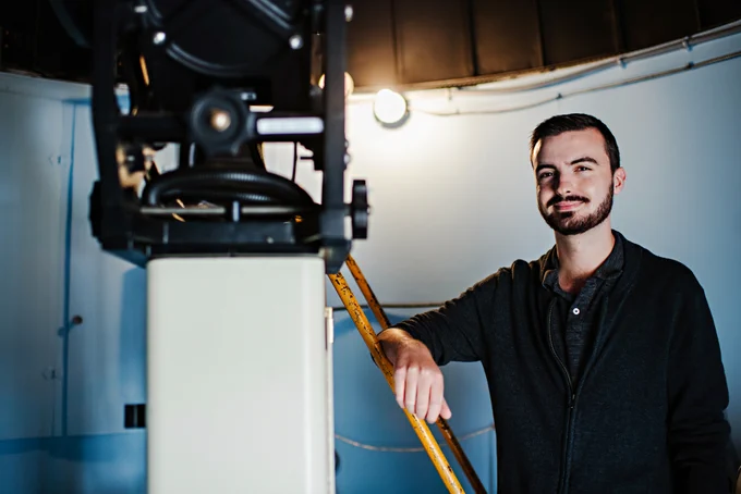 Cameron Morgan beside a telescope