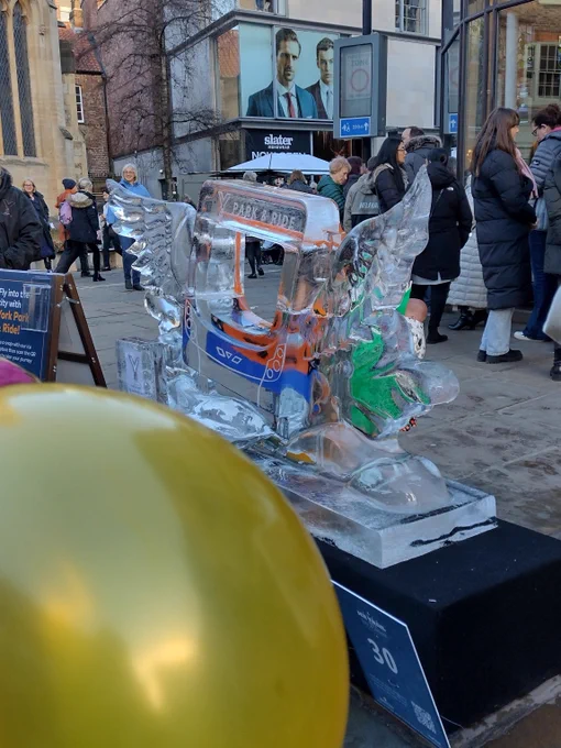 An ice sculpture of a bus with wings sits in the midst of a bustling crowd