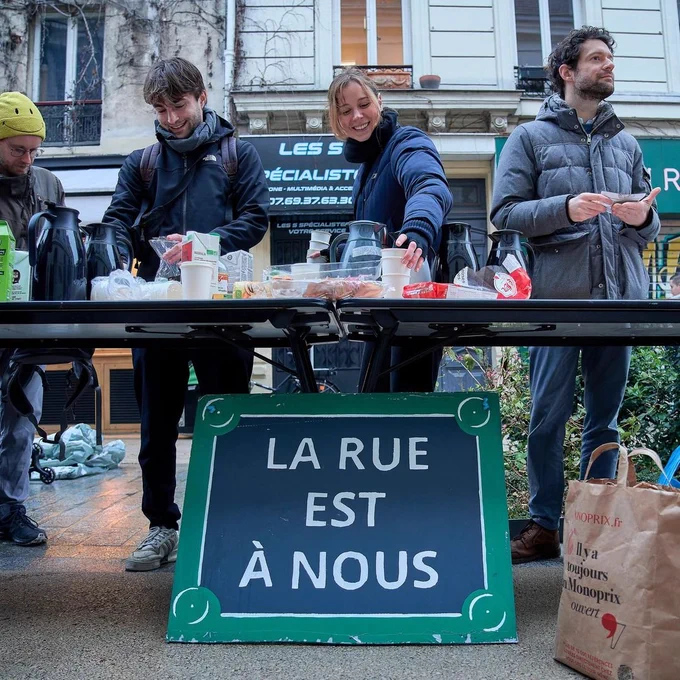 Foto mit Menschen an einem Tisch bei einer Infoveranstaltung in Paris unter dem Titel la Rue est a nous