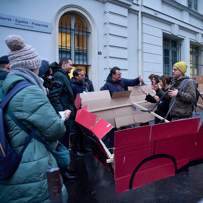 Menschen mit einem Gehzeug, einem Pappauto, bei einer Infoveranstaltung zum Voting über SUVs in Paris