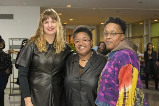 Three smiling women stand side by side. In the center is Jen Everett whose work centers butch black lesbian stories