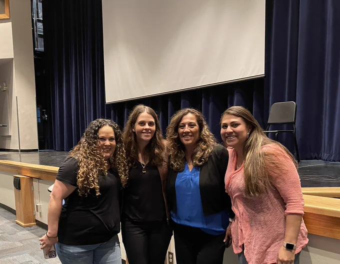 Four people, standing together and smiling, in a large auditorium.