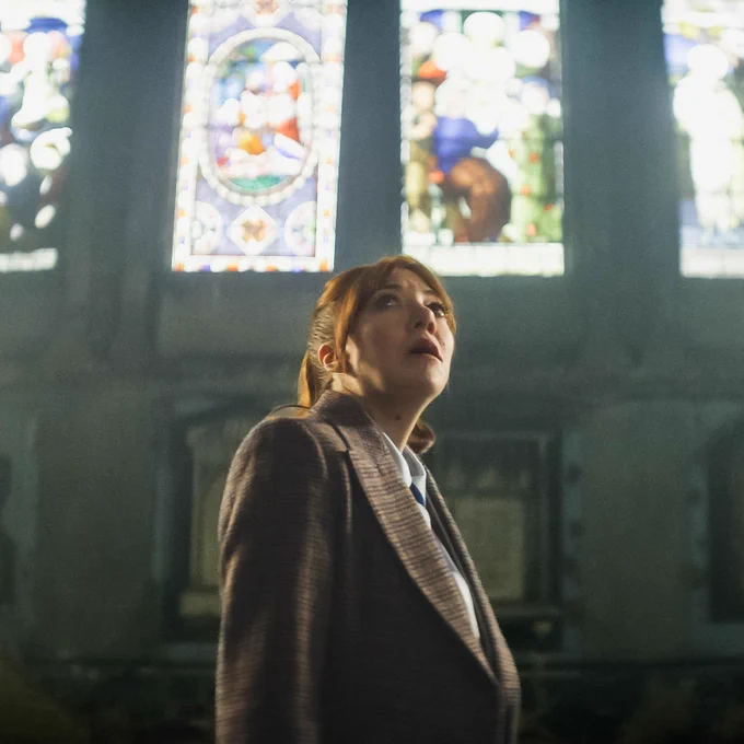 Philomena Cunk in a church, looking up. Light streams in through stained glass windows.