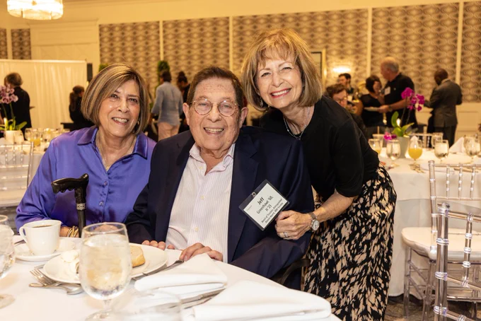 Three people seated at a table pose and smile.