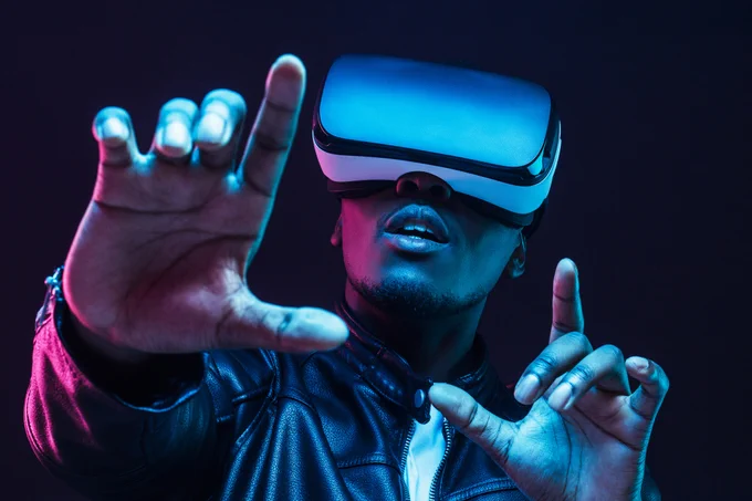 Young man wearing virtual reality goggles with hands up, isolated on black background