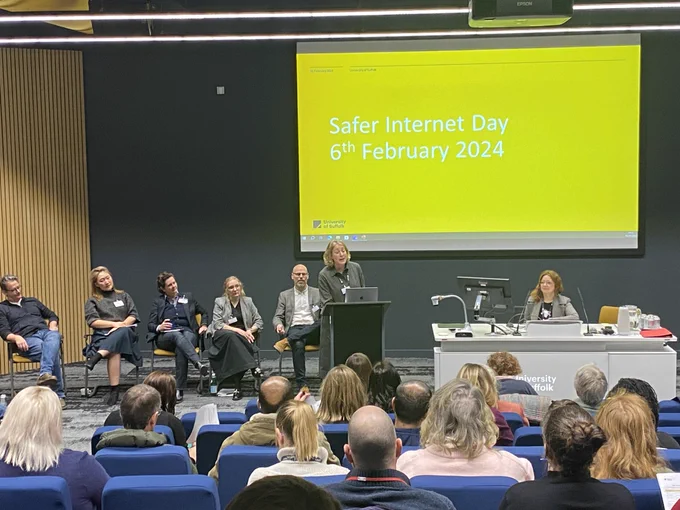 Professor Emma Bond speaking in a lecture theatre for the safer Internet day event. The front few rows of audience are visible in front of her, and the panel of speakers are seated behind her.