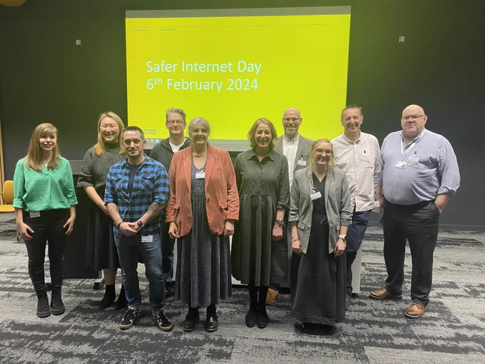 A group photo of the speakers for the Safer Internet Day event at the University of Suffolk. They are gathered at the front of the lecture theatre with the words 'Safer Internet Day, 6th February 2024' visible on the screen behind
