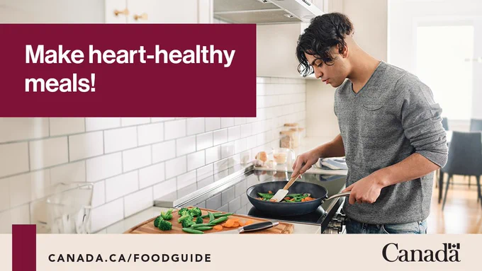 A person is sauteing carrots, peas and broccoli in a frying pan on the stove. There is a cutting board with a knife and some extra vegetables. Image text reads Make heart-healthy meals!

