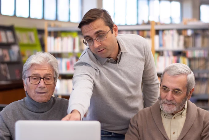 Two elders receiving computer help in a library.