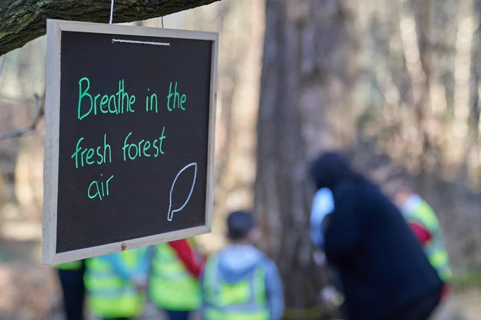 A sign saying breathe in the fresh forest air, with a group of children out of focus in the background 