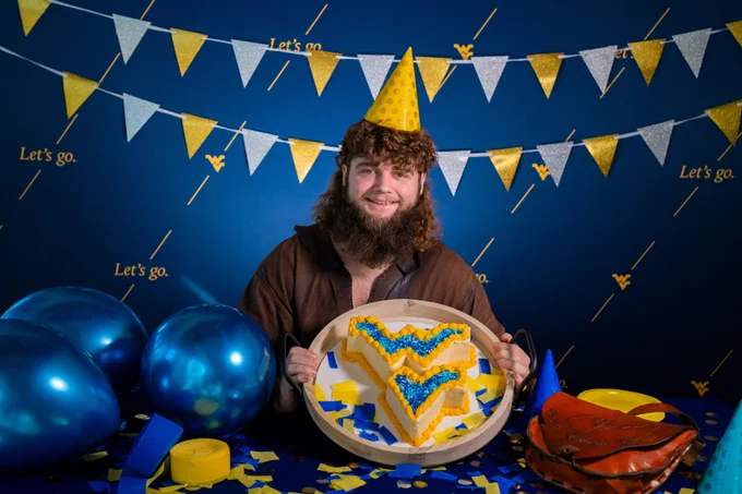 69th Mountaineer Mikel Hager holds a cake in the shape of the flying WV to celebrate WVU's birthday. 