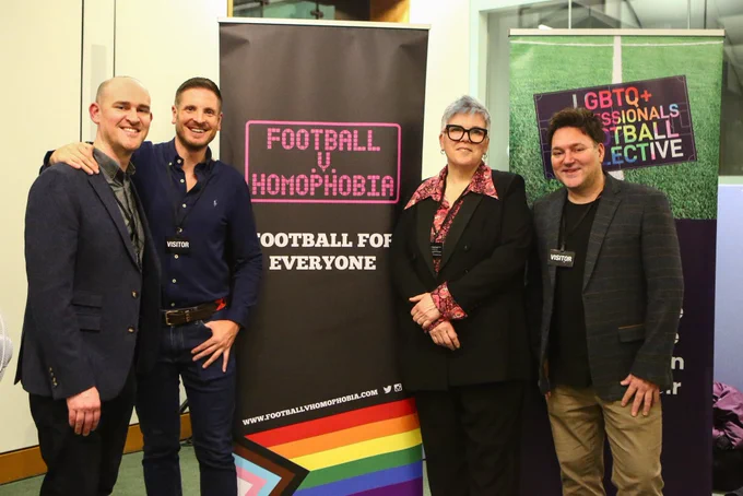 Jon Holmes, Ryan Atkin, Lou Englefield and Aubrey Crawley stand in front of a banner saying Football v Homophobia - Football for Everyone