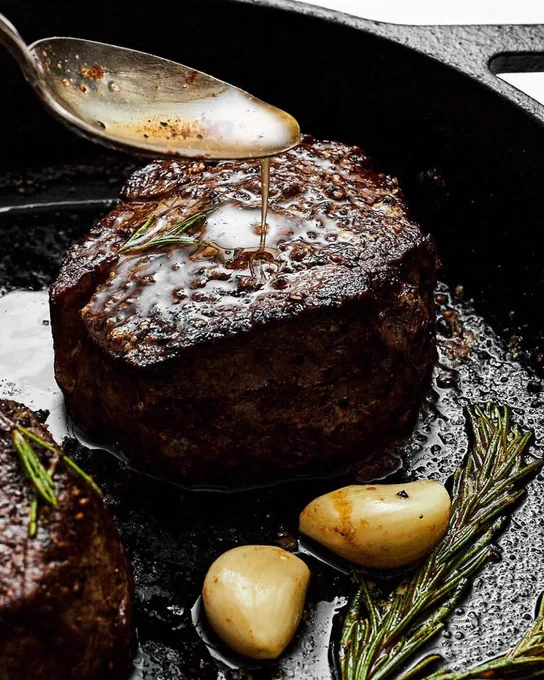 Filet mignon seared in a cast-iron skillet with garlic cloves and rosemary.