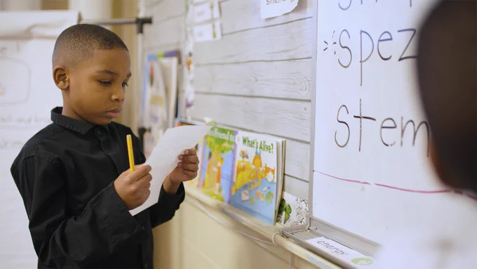 Image from the film "The Right to Read" - a young boy reading a paper in his hands.