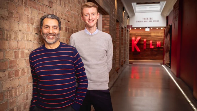 Amit Sharma and Iain Goosey, leaning against a brick wall with the Kiln sign in the background.