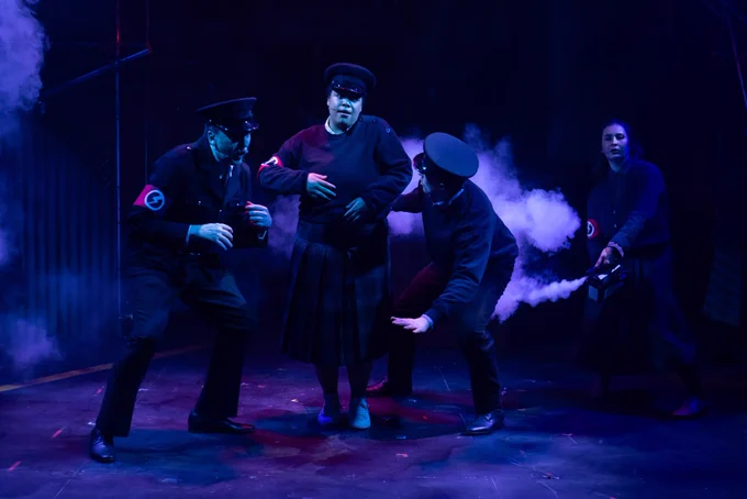 Three actors in BUF uniforms dance as another actor sprays them with smoke