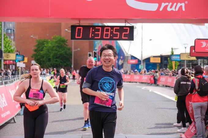 A man with glasses comes through the finish line of the Great Bristol Run with a smile on his face!