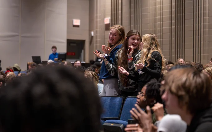 Three students stand up in a crowd.