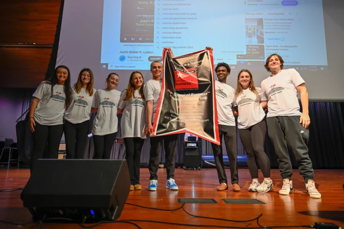 Eight students pose for a picture. Two of them hold a banner.