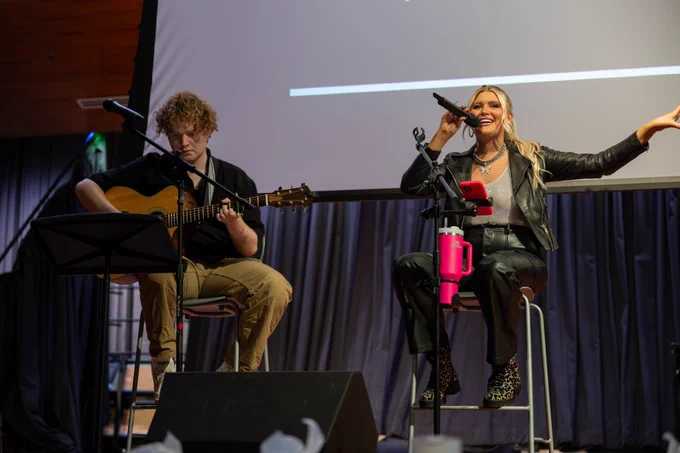 A person plays guitar while another one signs on stage.