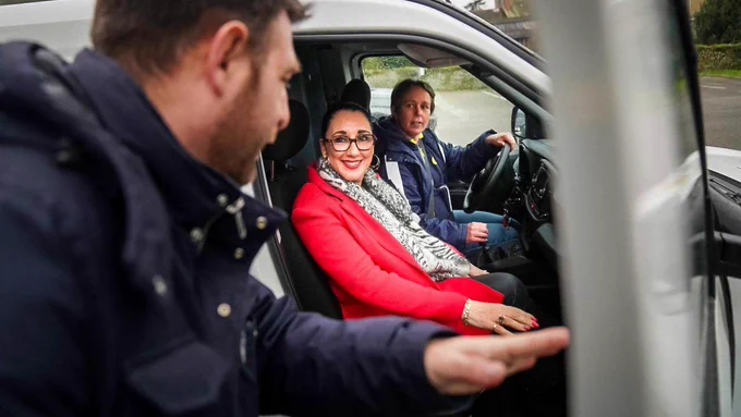 Fadila Khattabi est assise dans une camionnette de La Poste aux côtés de la factrice qui est au volant.

Au premier-plan, un homme tient la porte de la camionnette ouverte.