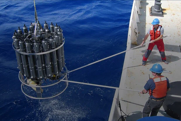 Scientists maneuver a conductivity, temperature, and depth sensor off the side of a ship.