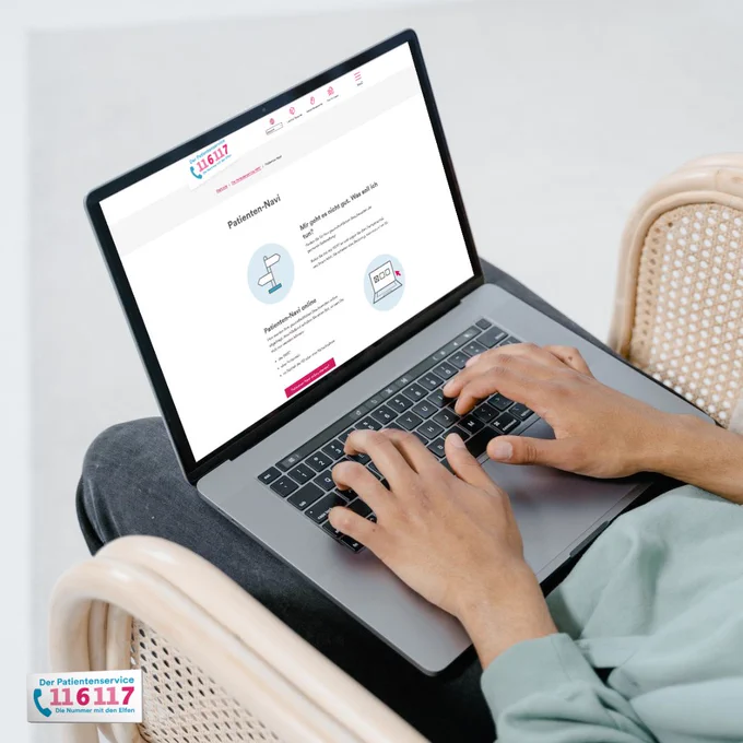 Ein Mensch sitzt mit Laptop auf einem Stuhl. Die Startseite des Bildschirms zeigt die Seite des Patientenservice 116117.