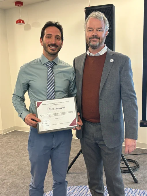Two adults standing together, smiling and holding the award certificate