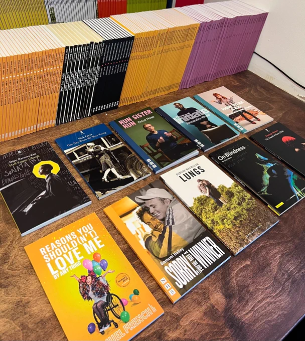 Ten playtexts laid out on a wooden surface. Behind those ten playtexts are shelves of further books!