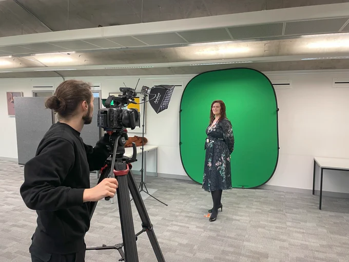 A photo of Ruth standing in front of a green screen being filmed