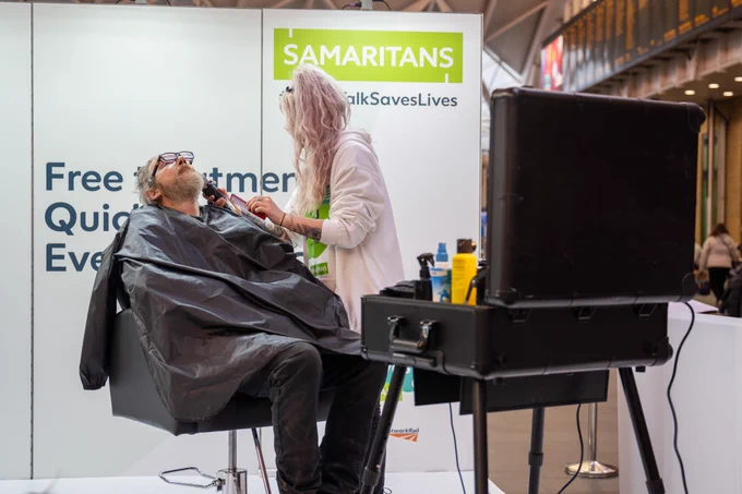 A man having his beard trimmed by a stylist as part of the Small Talk Saves Lives pop up salon on the concourse at King's Cross station.