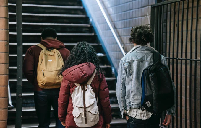 Three young people wearing backpacks walking up a flight of stairs.