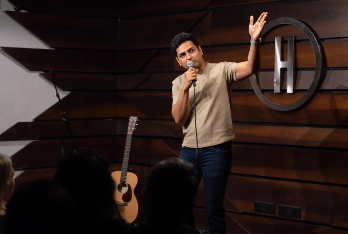 Kenny Sebastian performing on stage, holding a microphone, with a guitar next to him. 
