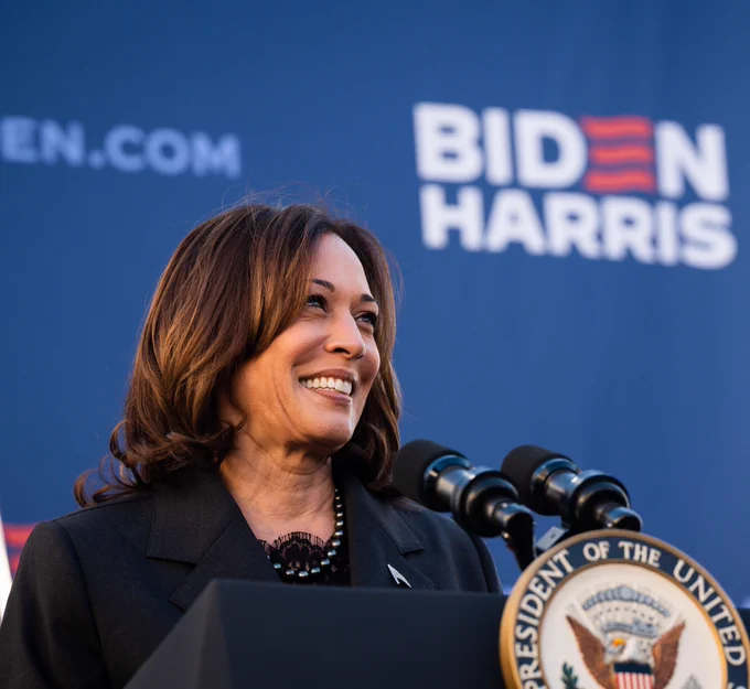 Vice President Kamala Harris smiling, standing behind a podium, with a Biden-Harris banner behind her.