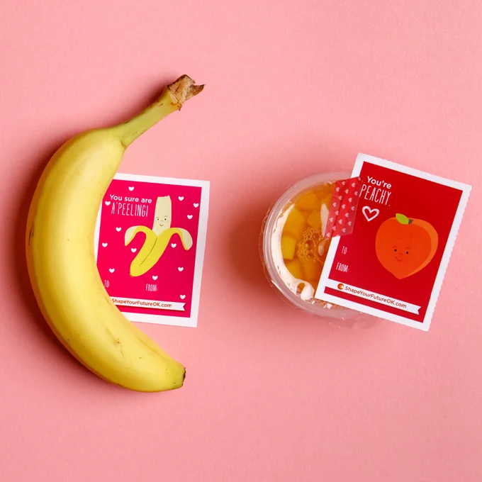 A banana and a peach fruit cup with Shape Your Future Valentine's next to them.