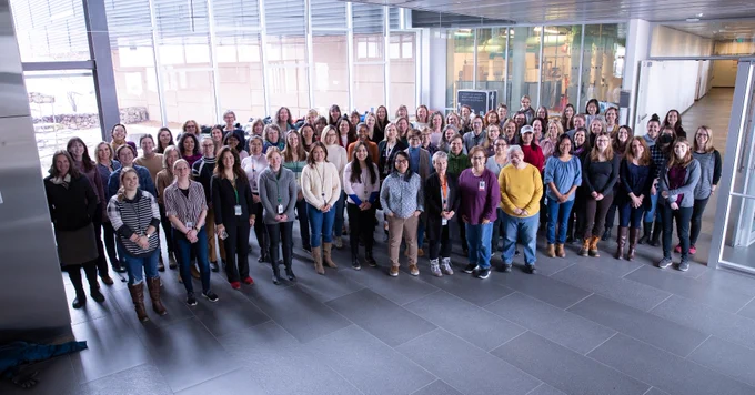 A massive group of women stands in the front lobby of a workspace.