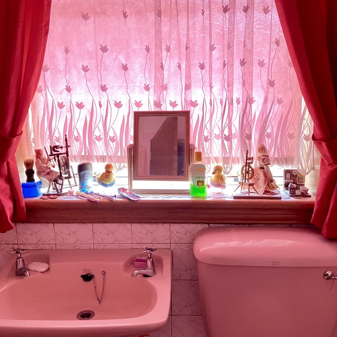 ‘In the Pink’ by Susan P. Mains. A photograph of a 1960s vintage pink bathroom suite with background light shining in through light pink lace window curtains.