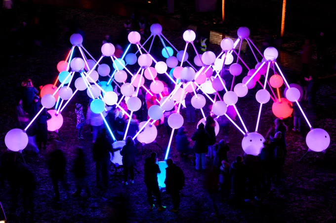 A night-time picture of a large art installation featuring large, interconnected balls of different shades of purple and blue. 