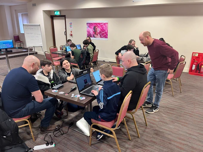 Adults and young people sitting at a table with laptops taking part in Astro Pi Mission Zero supported by the RPF team.