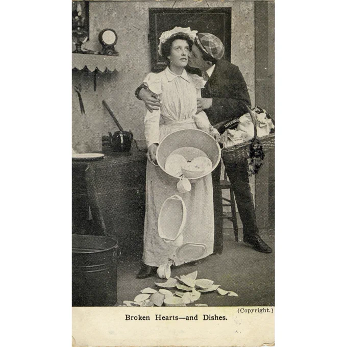 Black and white photo of a man kissing a woman on the cheek. She is spilling dishes from a bowl. The caption reads "Broken Hearts-and Dishes."