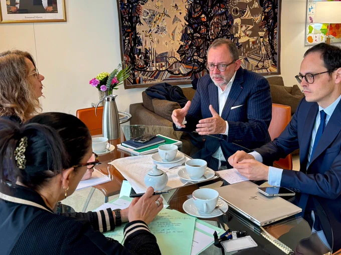 Luc Broussy et Fadila Khattabi échangent autour d’une table sur laquelle sont disposés des dossiers et divers objets. Ils sont accompagnés par leurs collaborateurs respectifs. Tous sont assis autour de la table.