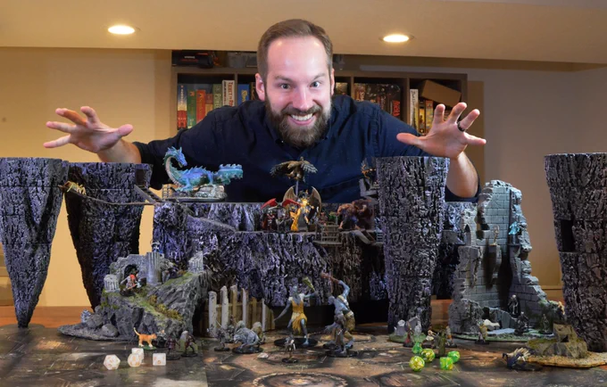 Me doing “master of puppets” hands over an elaborate terrain display with miniatures of giants, devils, and a dragon.